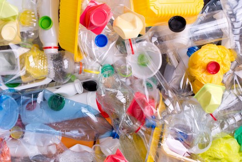 A close-up view of a pile of assorted waste plastic bottles and containers, including clear, coloured, andopaque plastics, some with caps still attached, scattered in a mixed arrangement. The bottles vary in size, shape, and colour, with some lying on their sides, leaning against each other, or stacked. Visible textures include smooth, glossy surfaces and crumpled edges, with some bottles appearing flattened or partially crushed. The background shows more plastic debris, creating a dense, chaotic appearance typical of waste awaiting removal. This scene is representative of rubbish collection efforts in residential or garden clearance contexts, highlighting the types of plastic waste managed by companies like Garden Clearance Havering. The natural lighting emphasizes the reflections and transparency of the plastics, underscoring the importance of proper rubbish disposal and recycling in the local Havering area, near London.